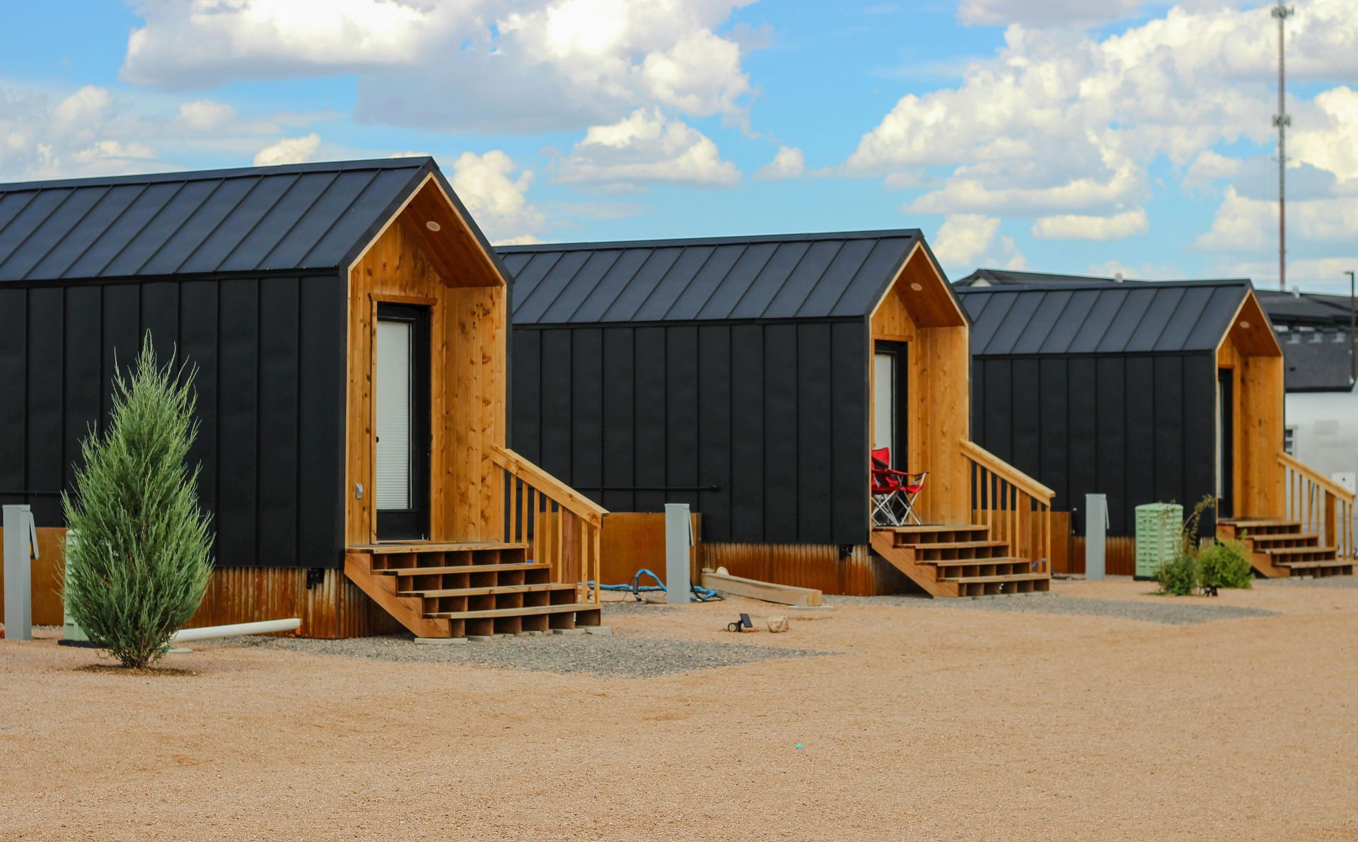 Modern black cabins with wooden porches in a gravel lot under a partly cloudy sky