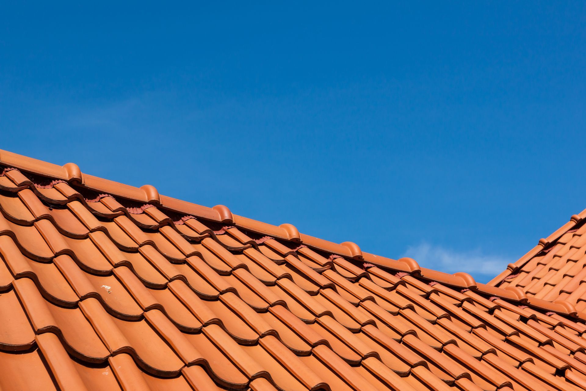 Gray shingled roof with a white brick chimney against a blue sky with clouds.