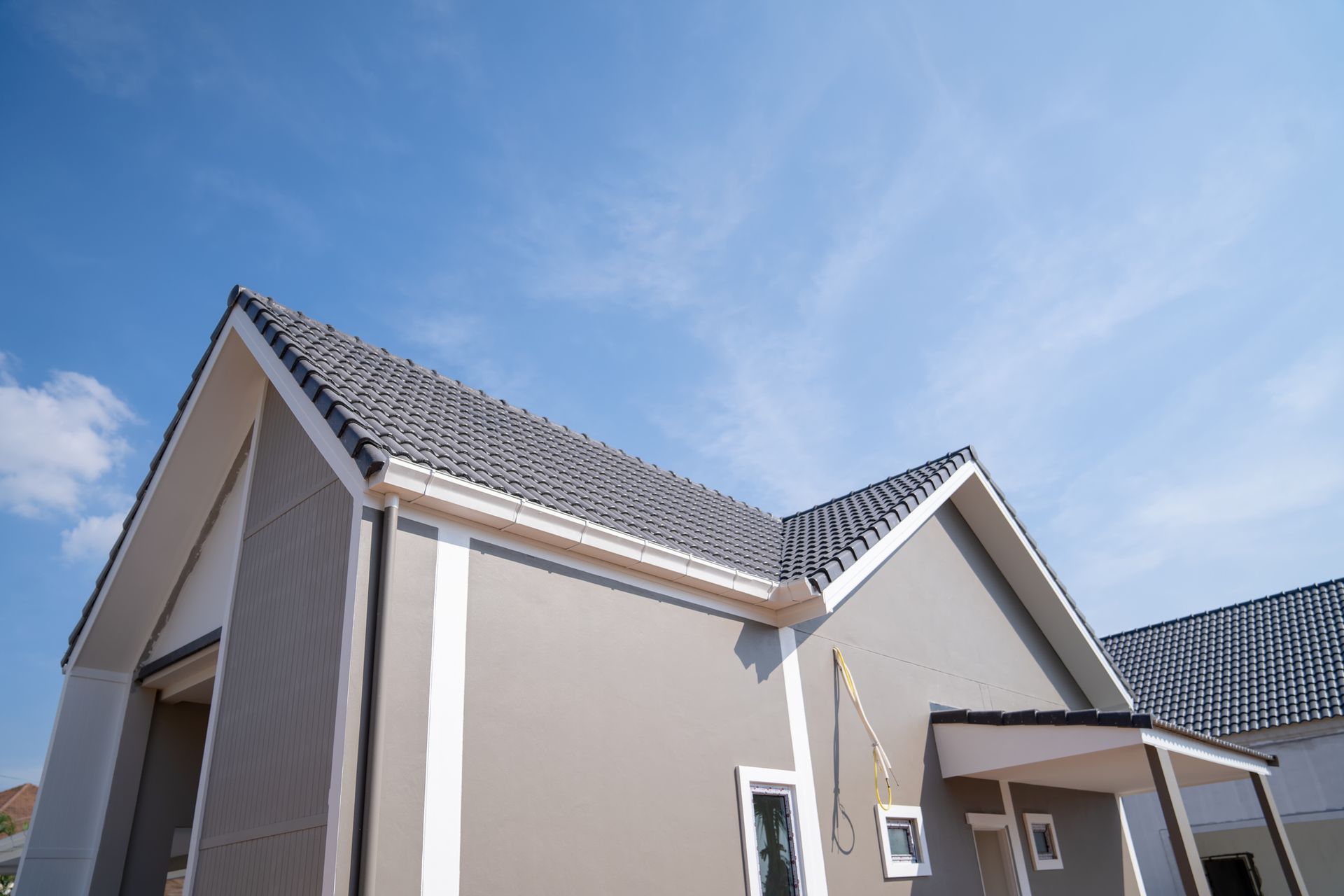 Gray shingled roof with a white brick chimney against a blue sky with clouds.