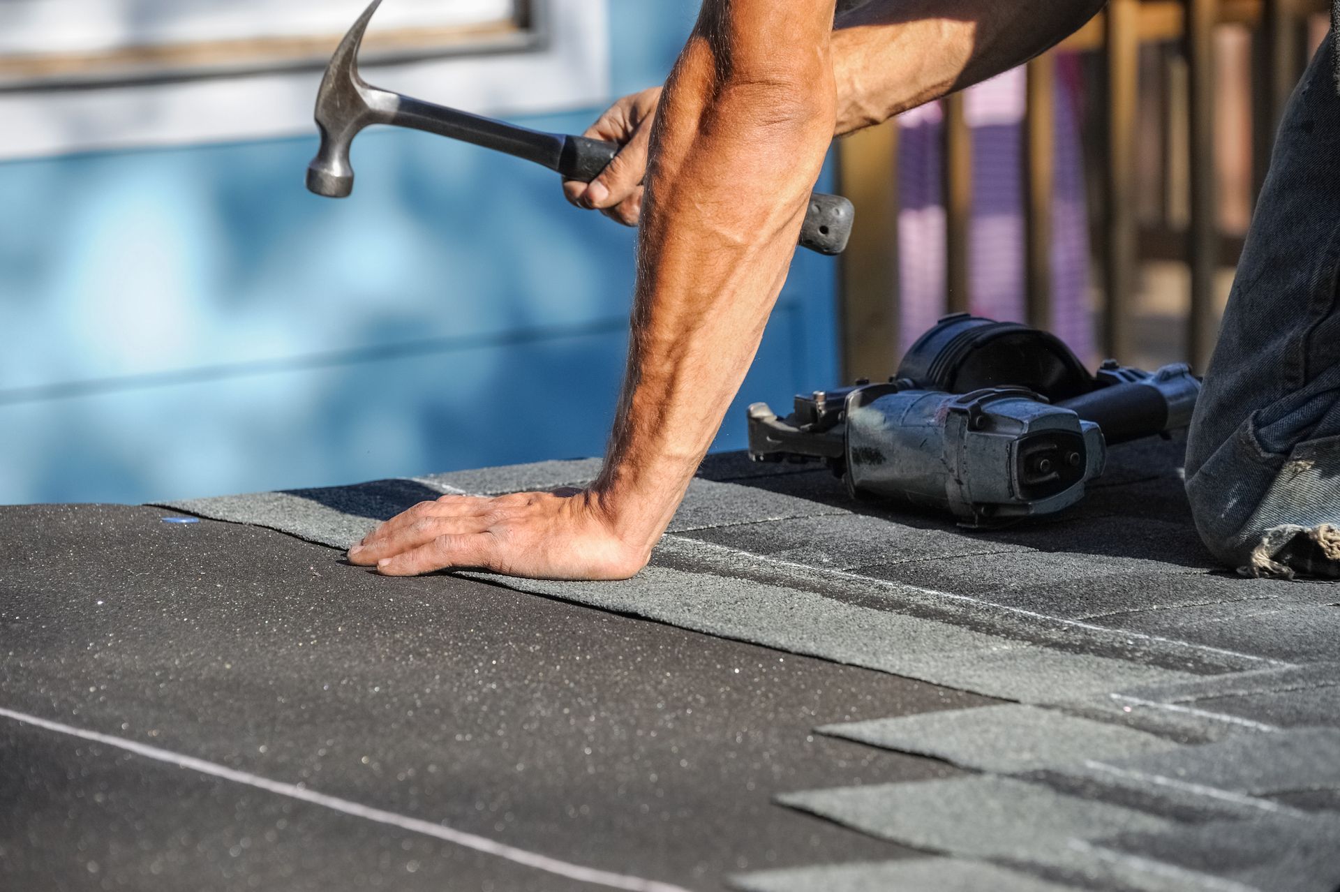 Person hammering shingles on a roof.