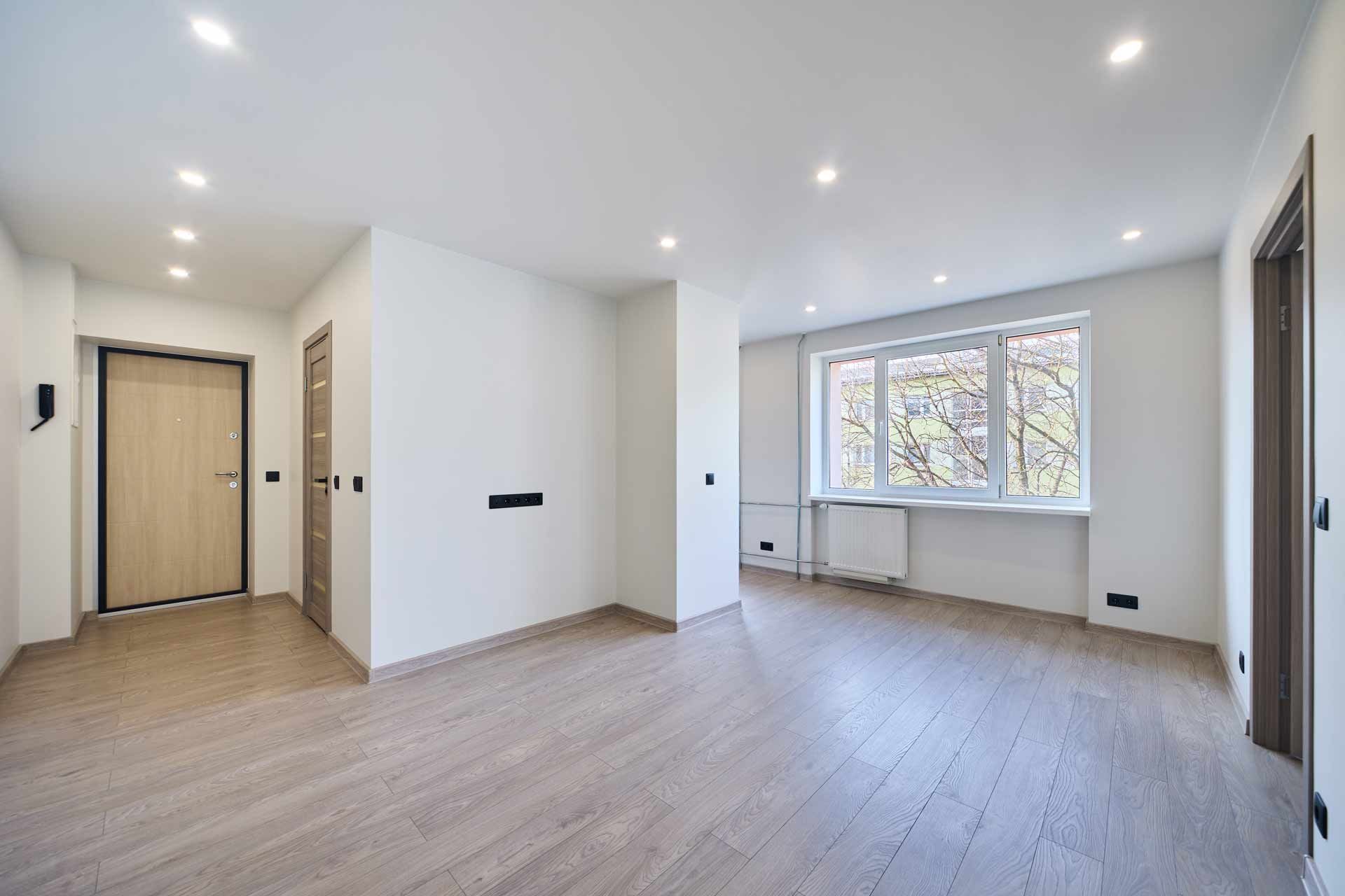 Bright empty modern apartment living room with light wood floors, white walls, and large windows