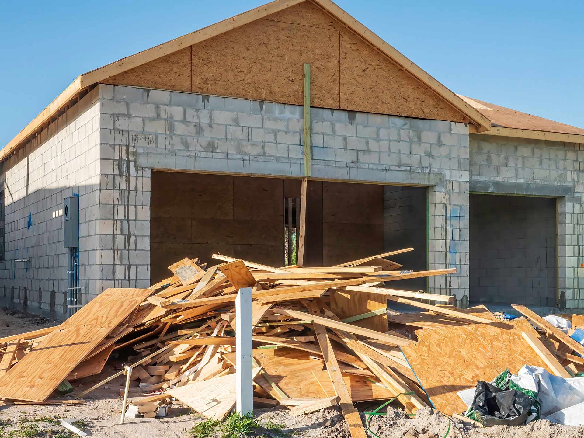 Partially built house with wood debris piled in front and unfinished walls under a clear sky