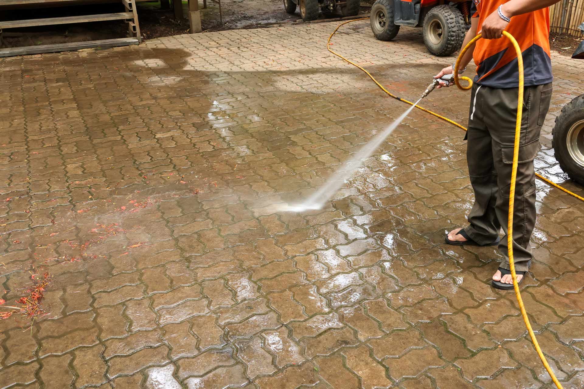 Worker pressure-washing a wet brick pavement with a hose outdoors
