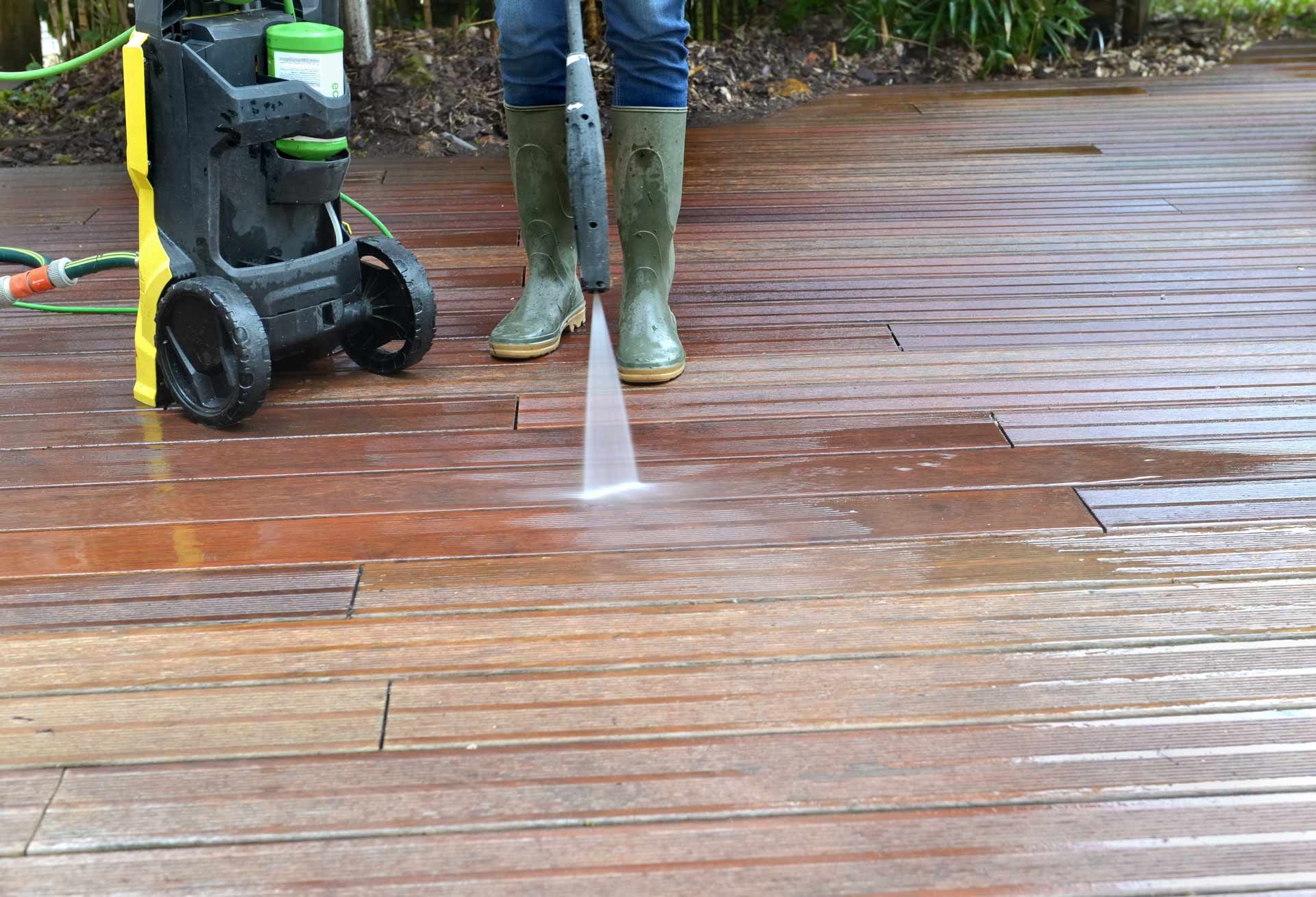 Person pressure-washing a wooden deck beside a black wheeled machine
