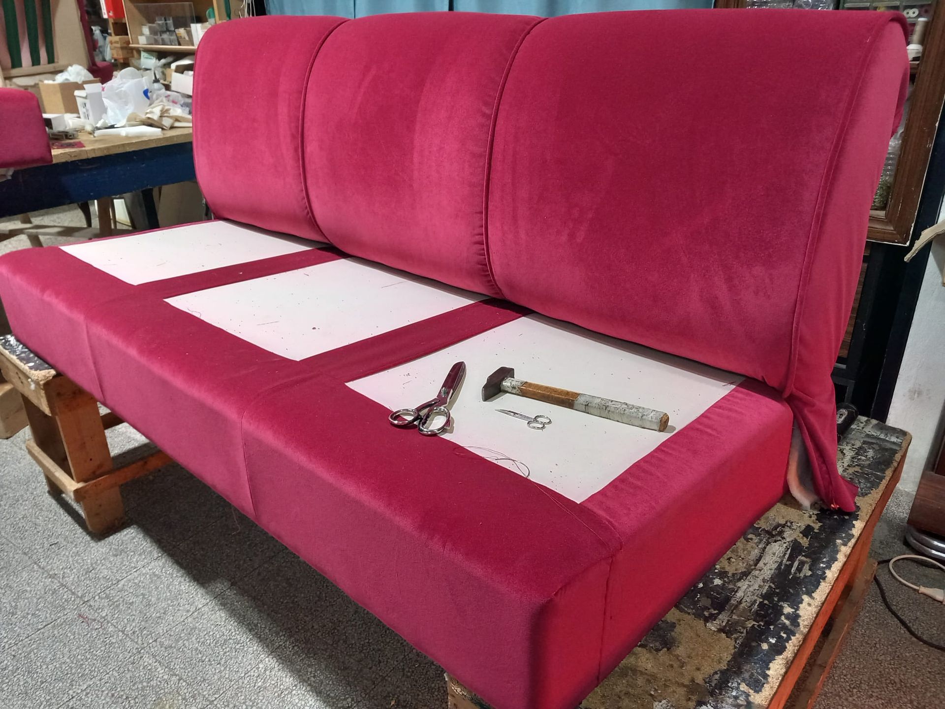 Un divano color magenta parzialmente imbottito, ambientato in un laboratorio. Sul sedile sono appoggiati alcuni attrezzi, tra cui forbici e un martello.