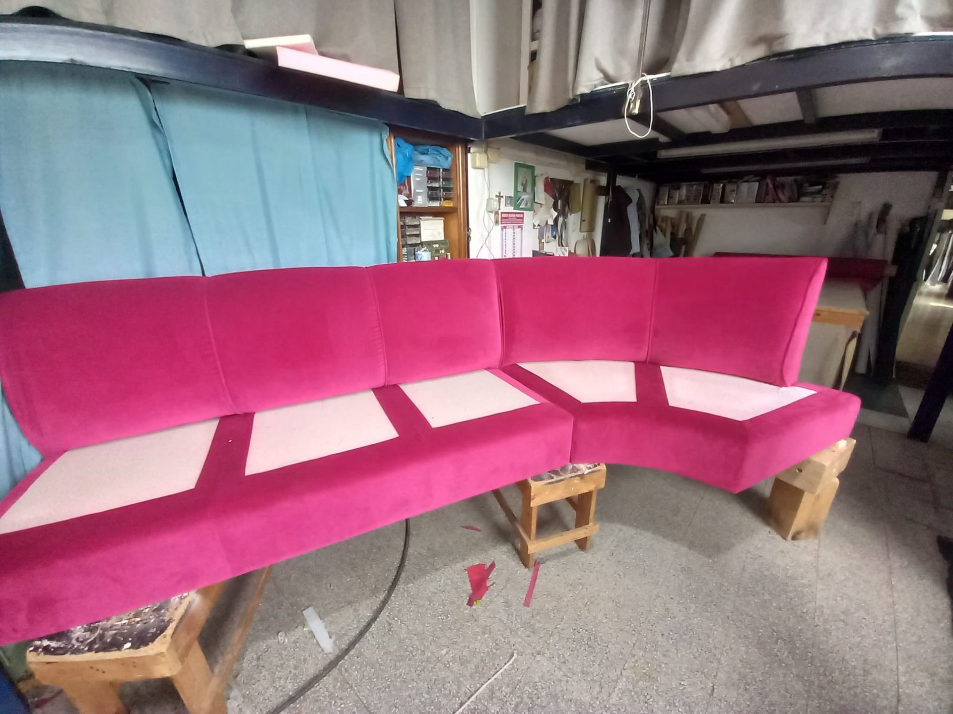 Un divano componibile in velluto magenta con cuscini rosa chiaro è appoggiato su supporti in legno in un laboratorio.