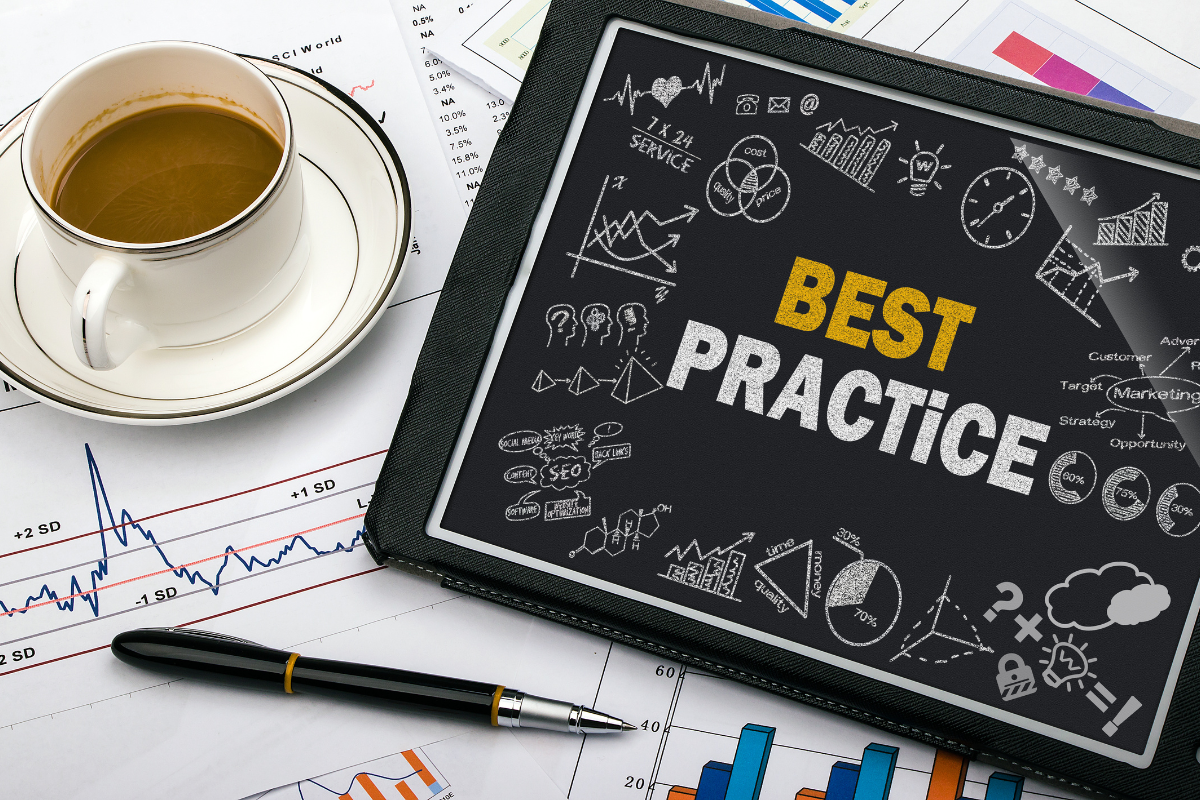 A cup of coffee and a pen next to a chalkboard featuring the phrase 'Best Practice' and its branches, illustrating best practices for PPC campaign optimization.