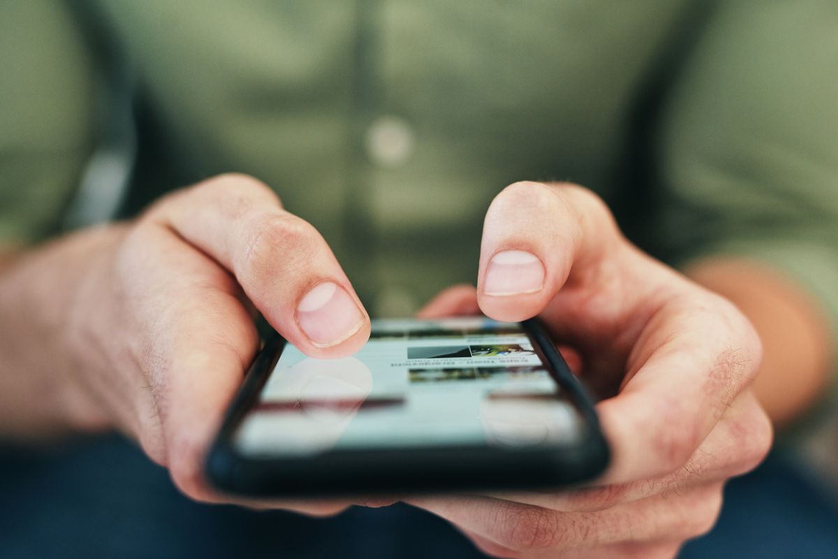Close-up of a person's hands using a smartphone for social media monitoring, with fingers scrolling through the screen.