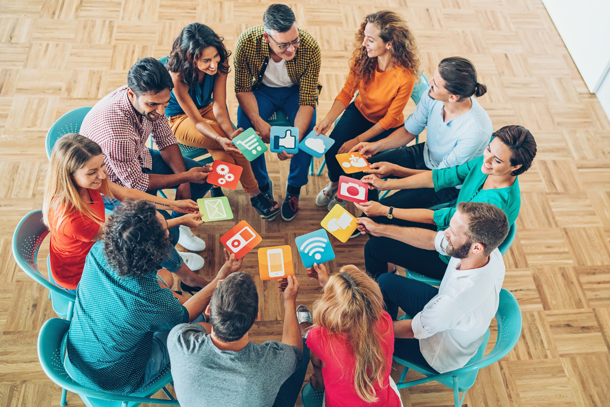 A group sits in a circle holding icons representing various apps, discussing social media monitoring and engagement.