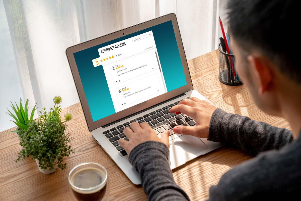 A person typing on a laptop displaying five-star customer reviews, representing online reputation management efforts.