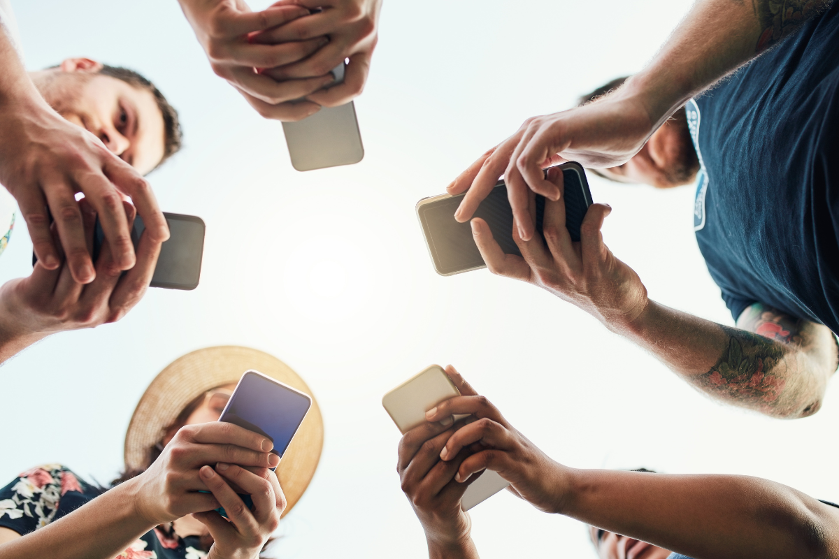 A group of people holding smartphones in a circle, engaging with shareable content from a low-angle perspective.