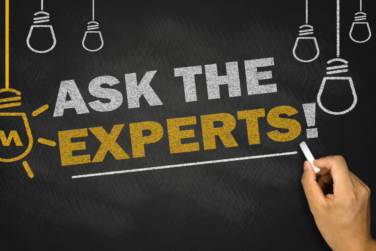 A hand writing 'Ask the Experts!' on a chalkboard with lightbulb illustrations, symbolizing expert advice and insights.