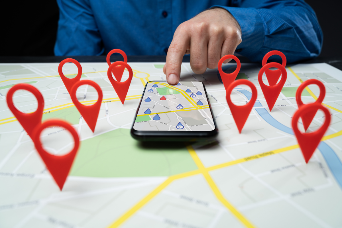 A person interacting with a smartphone map app, surrounded by red location pins on a printed map, symbolizing rankings.