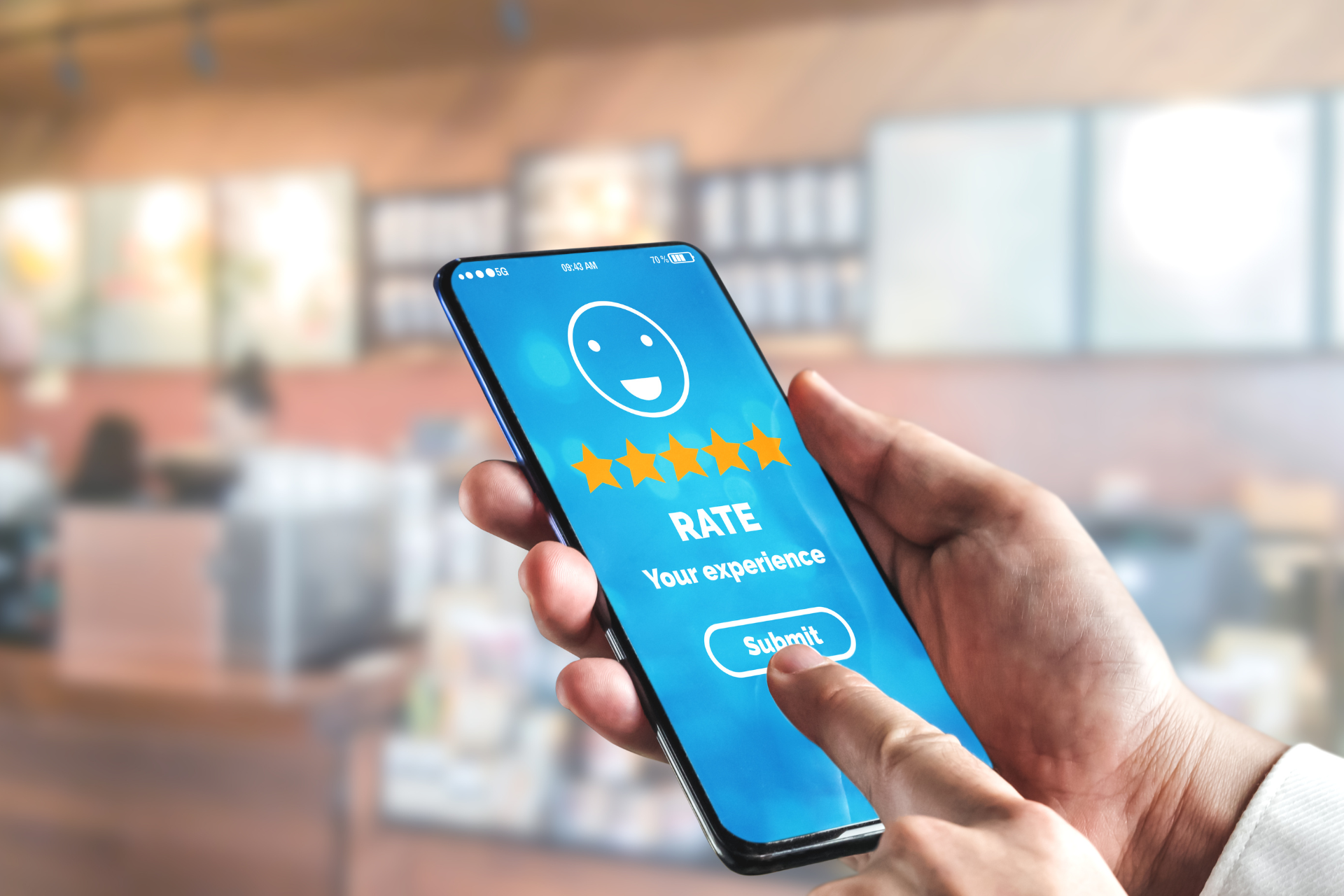 A person using a smartphone to give a 5-star rating and submit feedback on their experience in a blurred café setting.