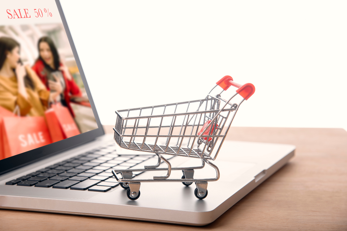 A miniature shopping cart on a laptop with a sale ad, symbolizing online shopping on fast fashion websites.
