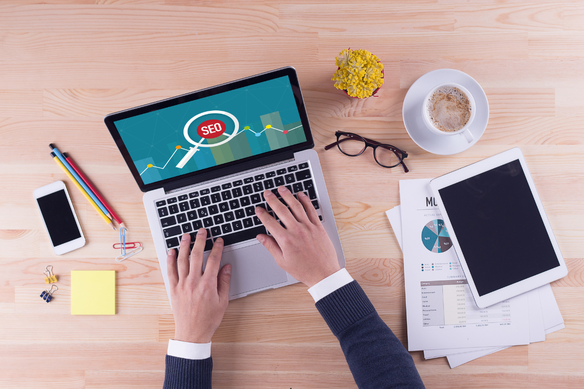 Person working on a laptop with an SEO graph on the screen, surrounded by tools, showcasing innovative SEO trends.