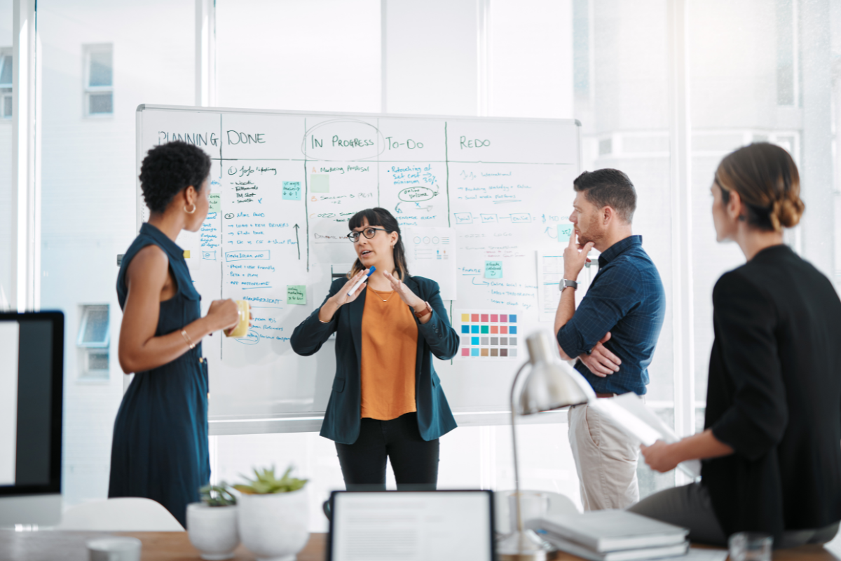 A group of people gathered around a whiteboard, collaboratively analyzing and optimizing growth marketing efforts, showcasing teamwork in strategy development.