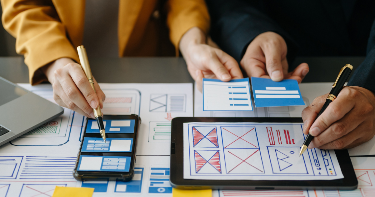 Designers planning a website layout on paper, tablet, and phone, illustrating user experience for healthcare SEO​.