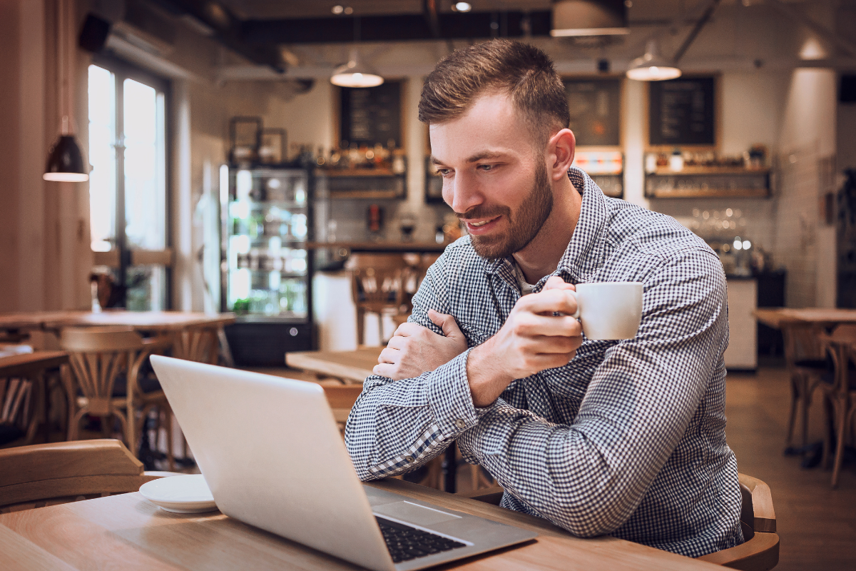 A man sitting at a table with a laptop and a cup of coffee representing the concept of personalized blog writing by tailoring content to your audience.