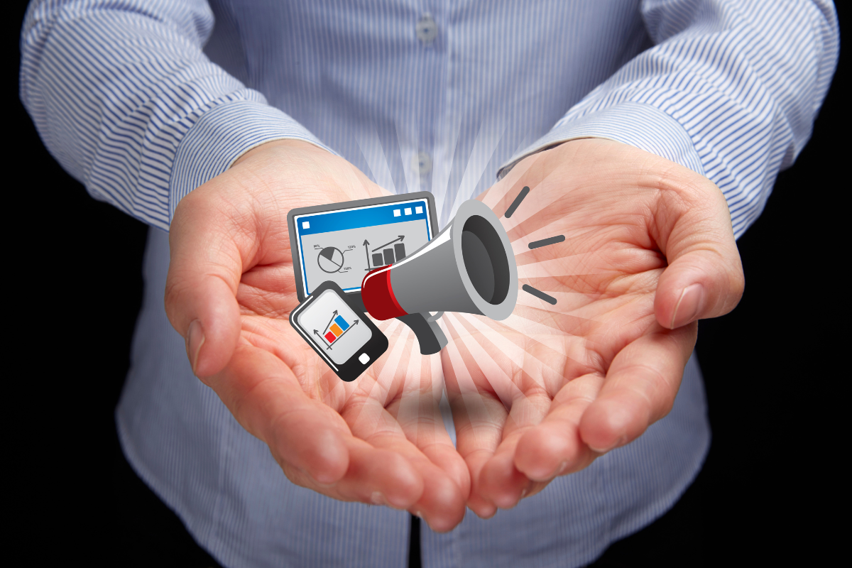 Hands holding icons of a megaphone, smartphone, and analytics, symbolizing digital marketing and outreach through mobile devices.
