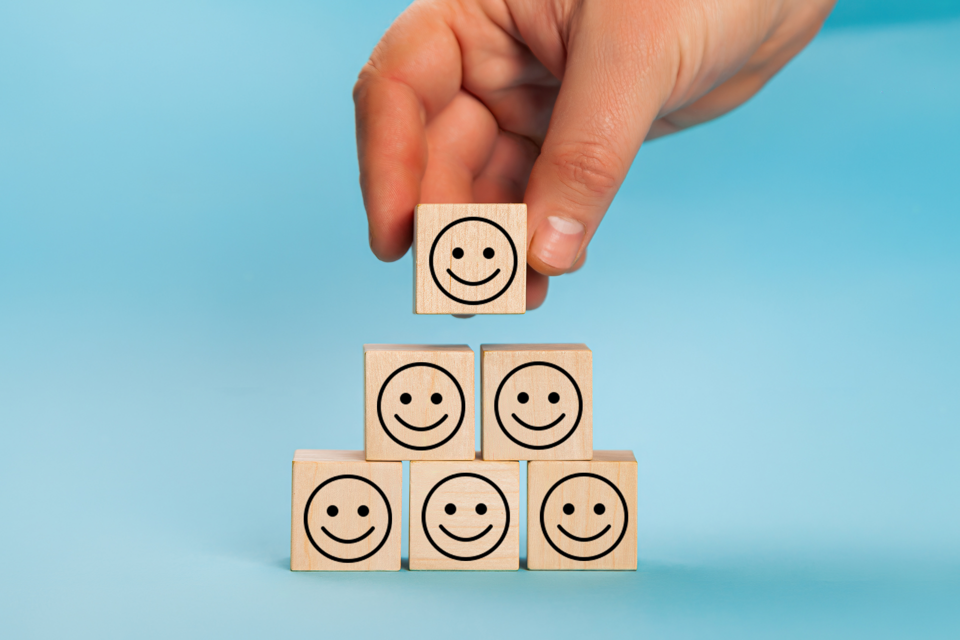 A hand stacks wooden blocks with smiley faces, symbolizing building positive customer experiences and strong brand reputation.