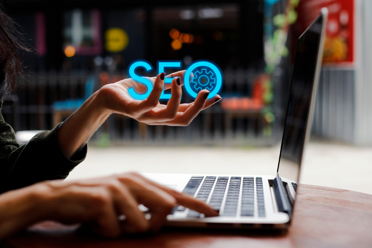 Hand holding a glowing 'SEO' icon near a laptop, representing scalable SEO trends and digital optimization strategies.