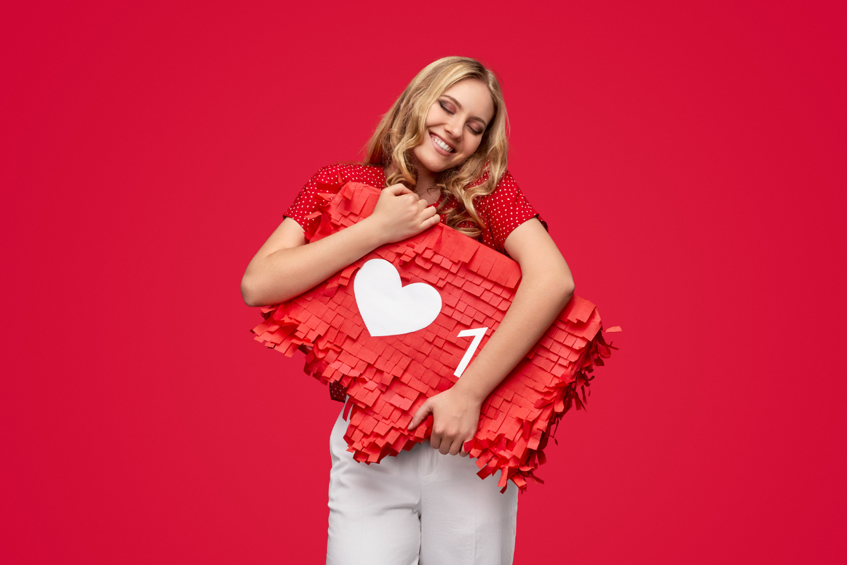 A smiling woman in red hugs a large social media like icon, symbolizing the power of shareable content and engagement.