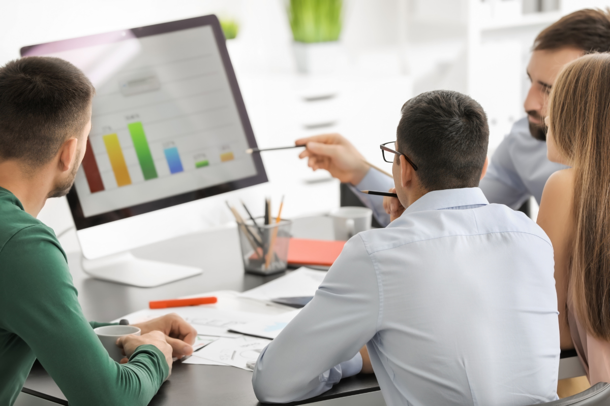 A group of SEO experts gathered around a computer screen, discussing strategies to boost visibility and drive results related to SEO conversions.