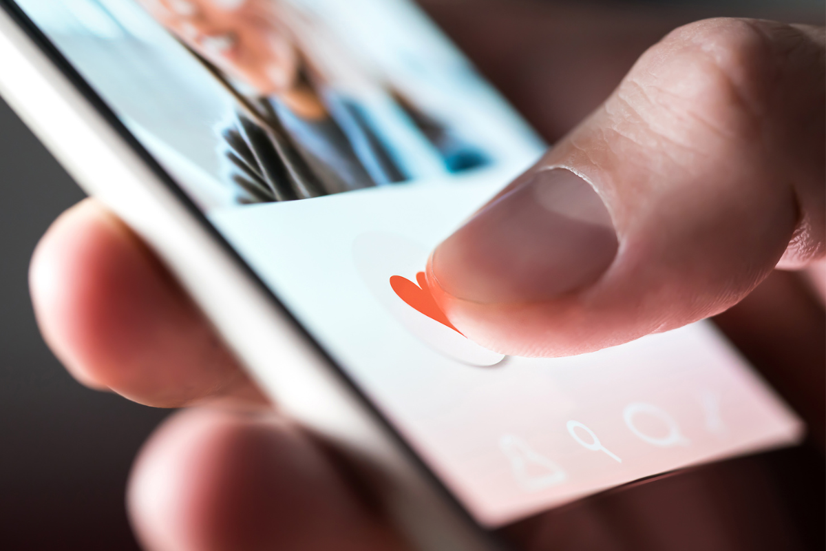 A hand tapping a heart icon on a smartphone screen, symbolizing engagement and connection on social media platforms.