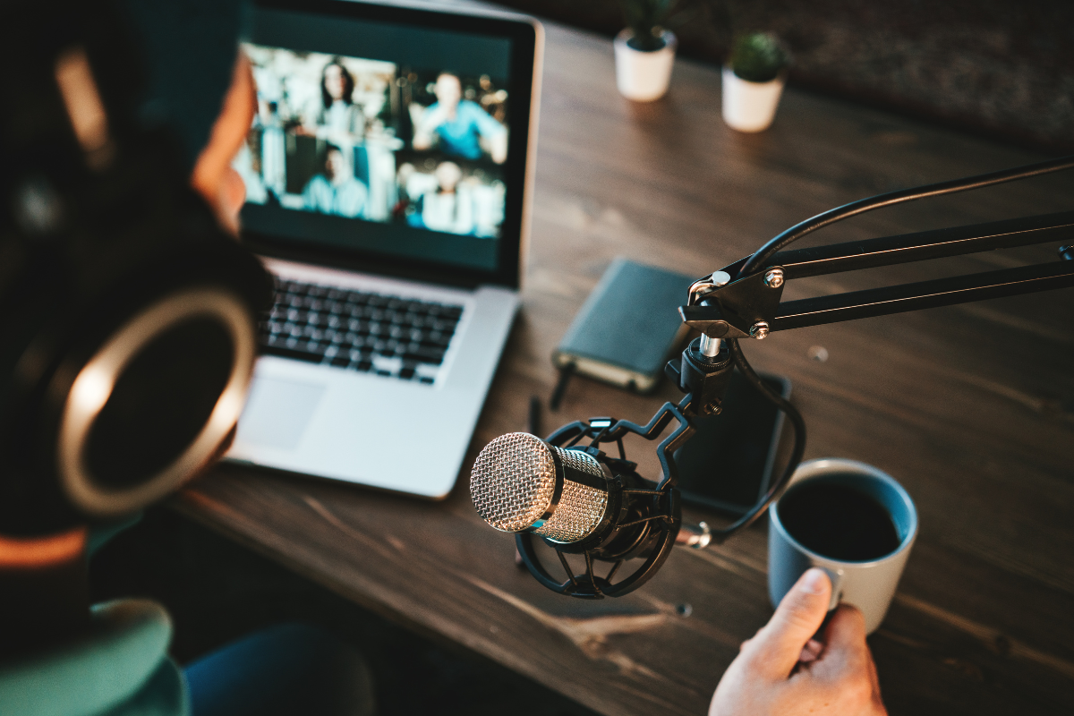 A person wearing headphones speaks into a microphone while video conferencing on a laptop.