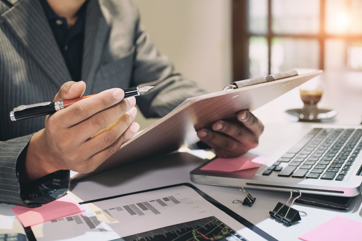 Person reviewing content audit results on a clipboard with charts, next to a laptop and documents on a desk.