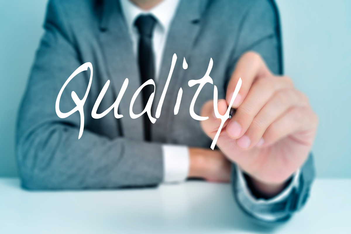 A businessperson in a suit writing the word 'Quality' on a transparent surface, emphasizing a focus on quality standards.