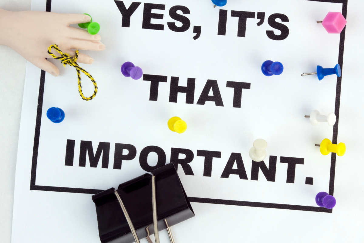 A hand holding a paper pinned to a board with the phrase 'Yes, It's That Important,' symbolizing the significance of blog writing in sharing ideas and delivering valuable content.