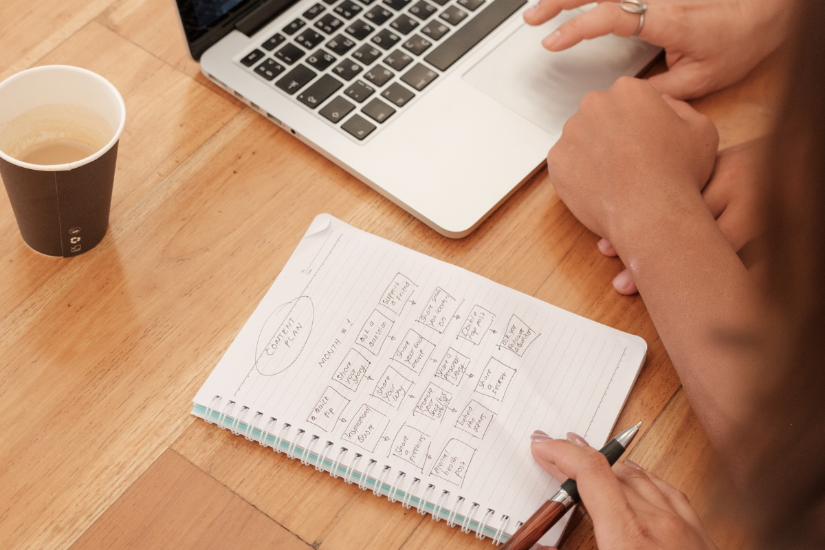 A person writing a content plan in a notebook, illustrating the strategic relationship between content marketing and SEO in driving online visibility and engagement.