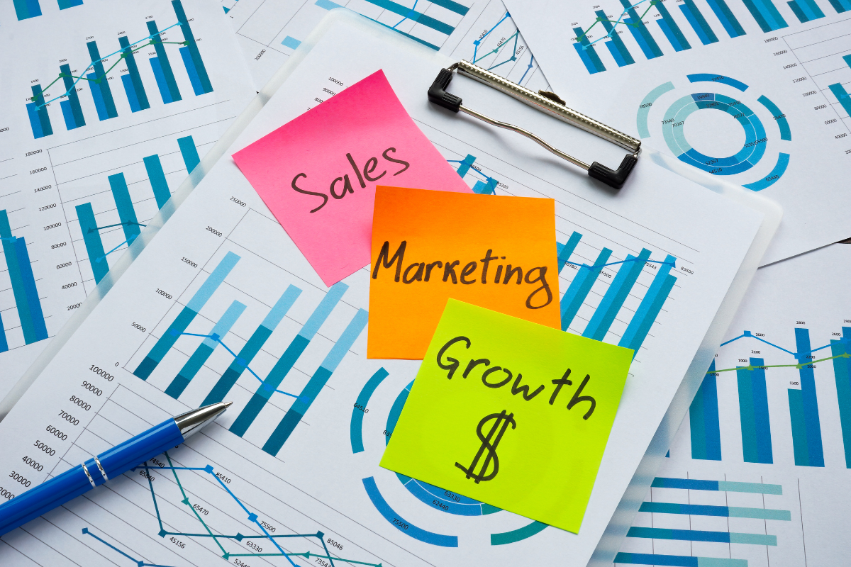 A bundle of papers displaying analytics, surrounded by notepads filled with notes on sales, marketing, and growth, illustrating concepts related to growth marketing.