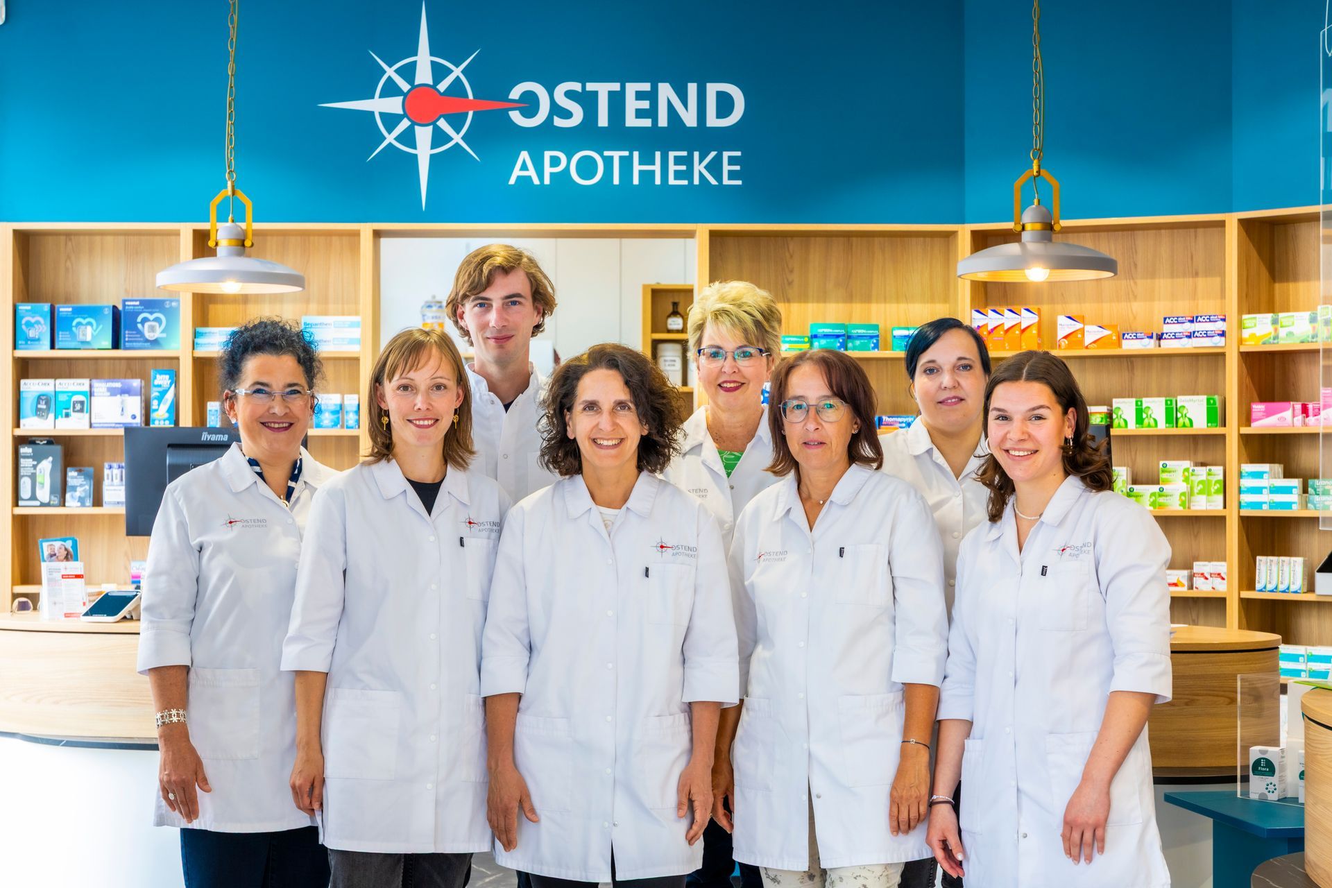 Eine Gruppe von Mitarbeiter*innen posiert für ein Foto vor einem Schild mit der Aufschrift „Ostend Apotheke“