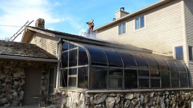Man power washing the exterior of a building with a hose, water spraying.