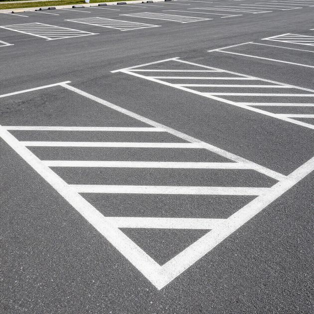 Parking lot with painted white diagonal lines and a striped accessible parking space.