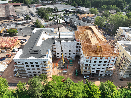 Aerial view of two apartment buildings under construction with cranes and surrounding trees