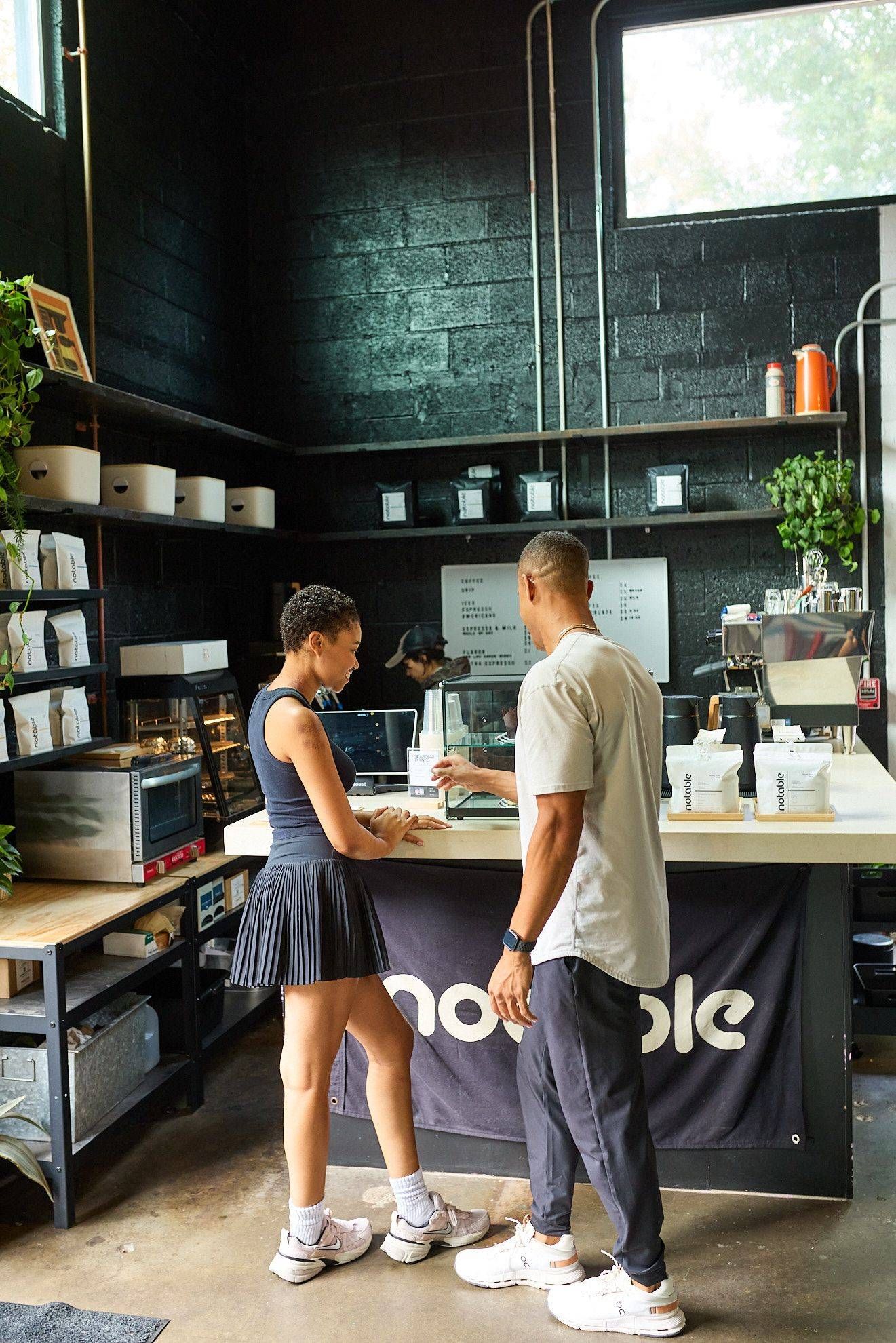 Two people standing at a café counter in a bright, modern coffee shop