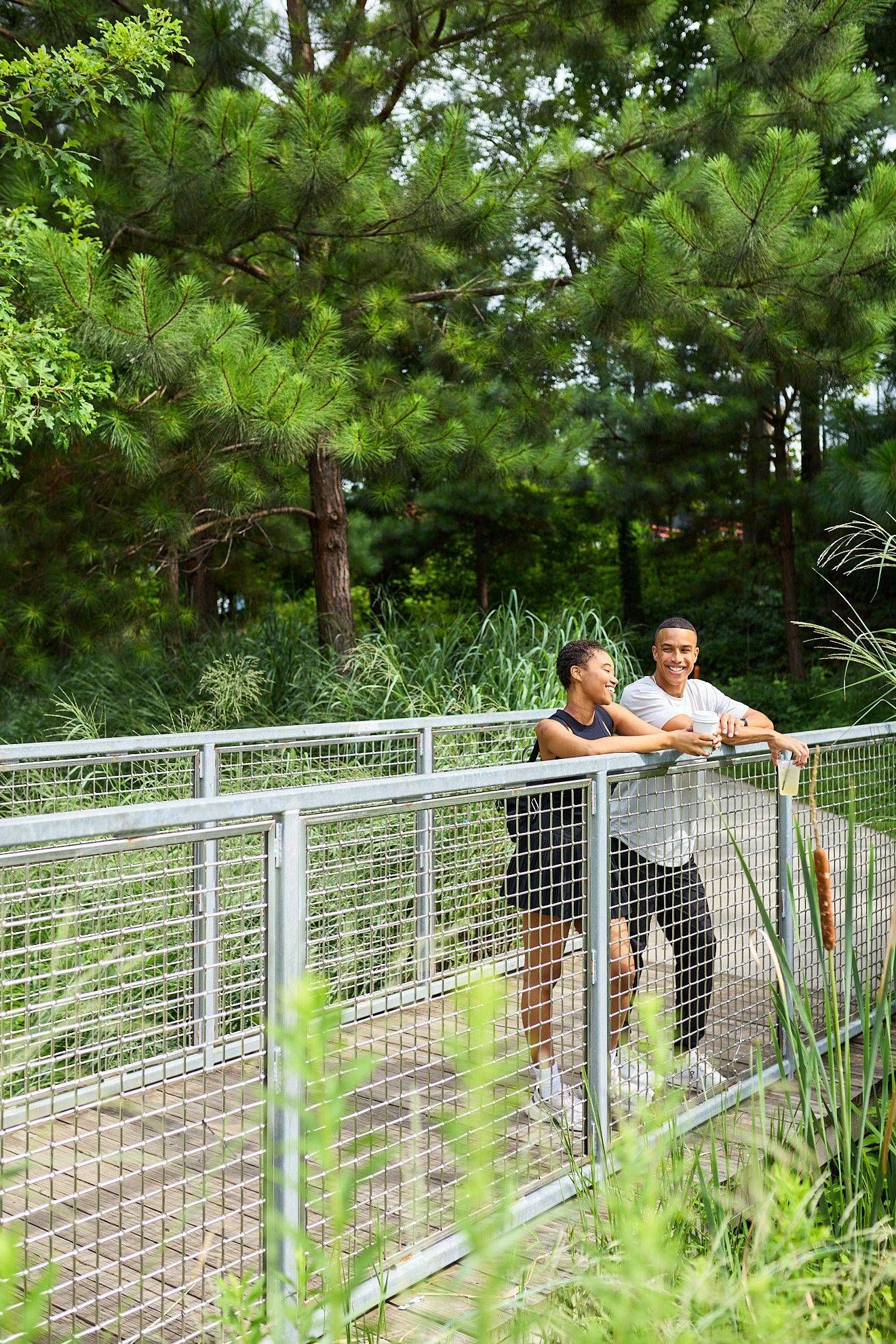 Two people leaning on a metal railing in a leafy park