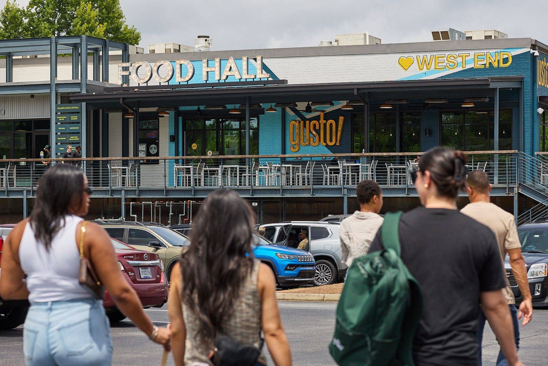 People walking past a Food Hall and grocery storefront with outdoor seating and parked bikes.