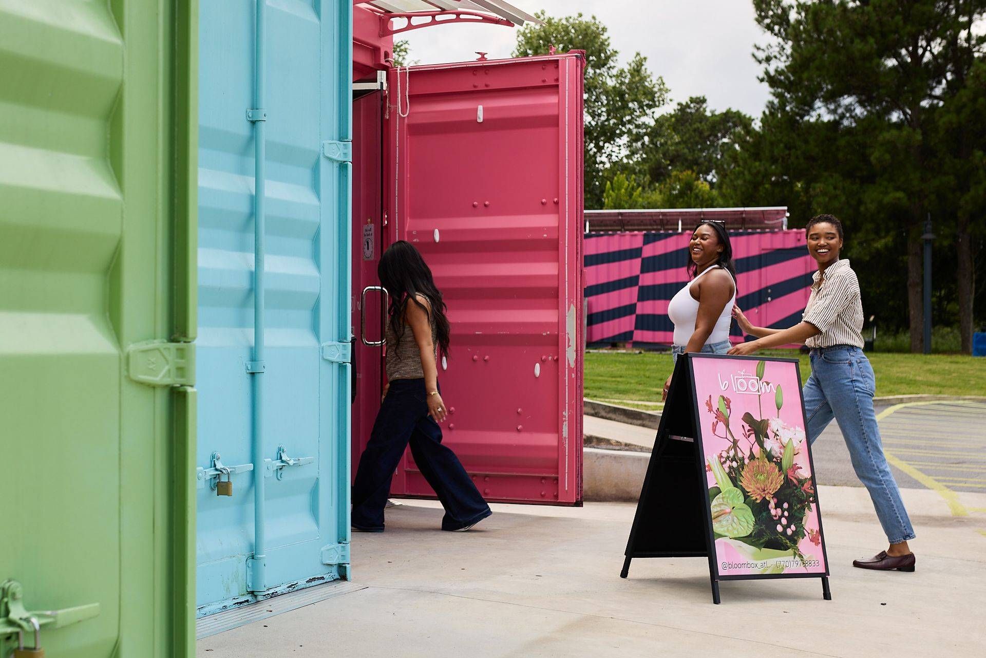 People walking near colorful shipping containers and a pink sign at an outdoor event