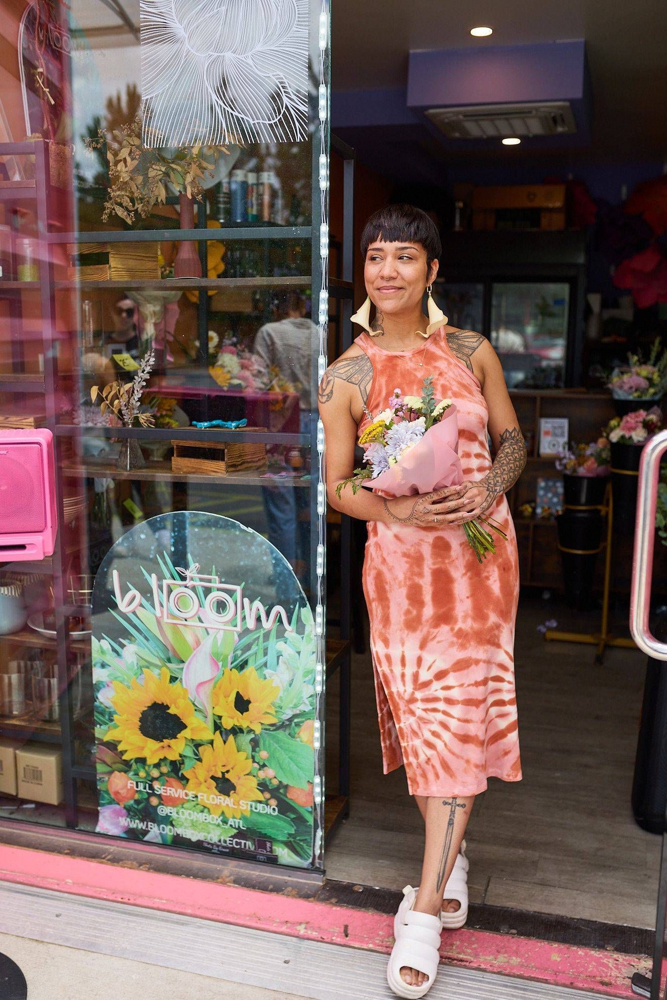 Woman in a coral dress standing in a shop doorway with a floral glass panel.