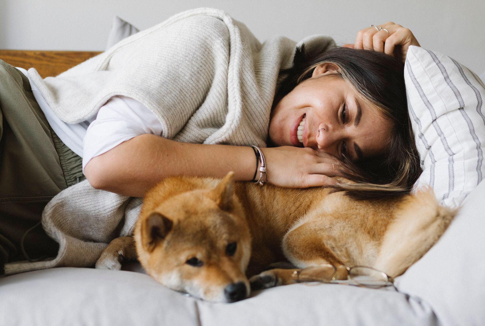 Woman lying on a couch, smiling while hugging a tan dog under a light blanket