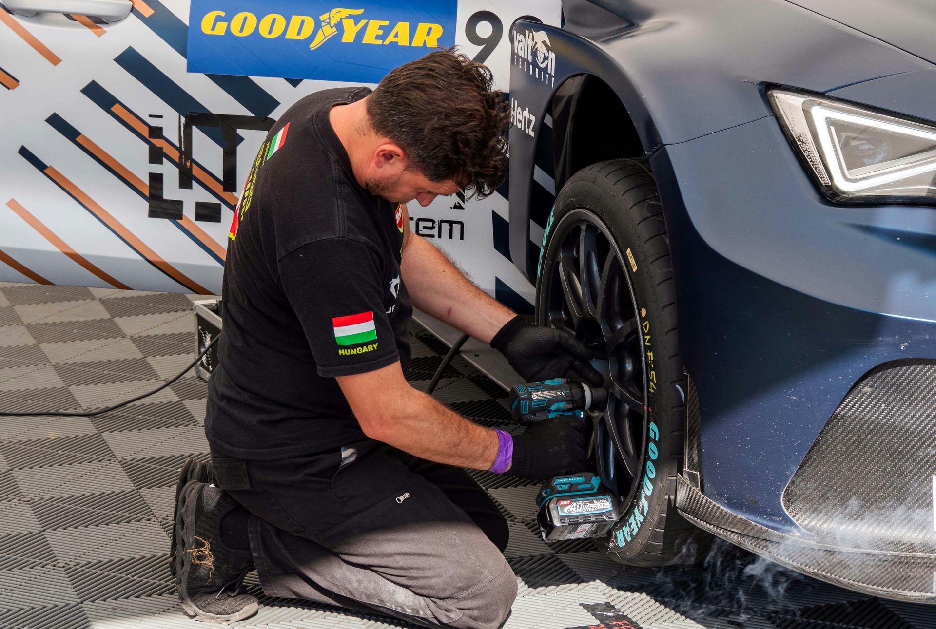 A man is kneeling down in front of a car with a good year logo on it.