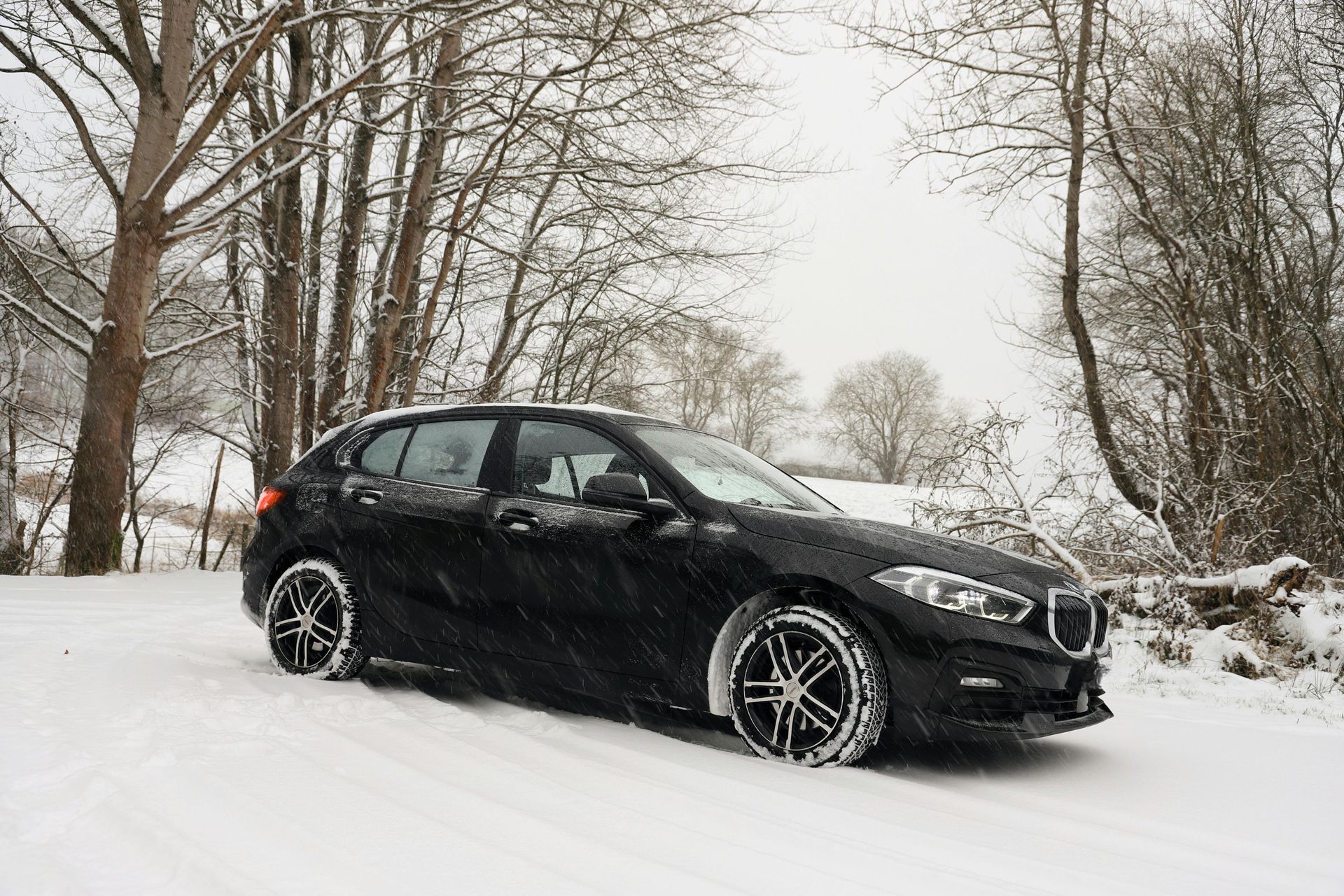 A black car is parked in the snow near trees.