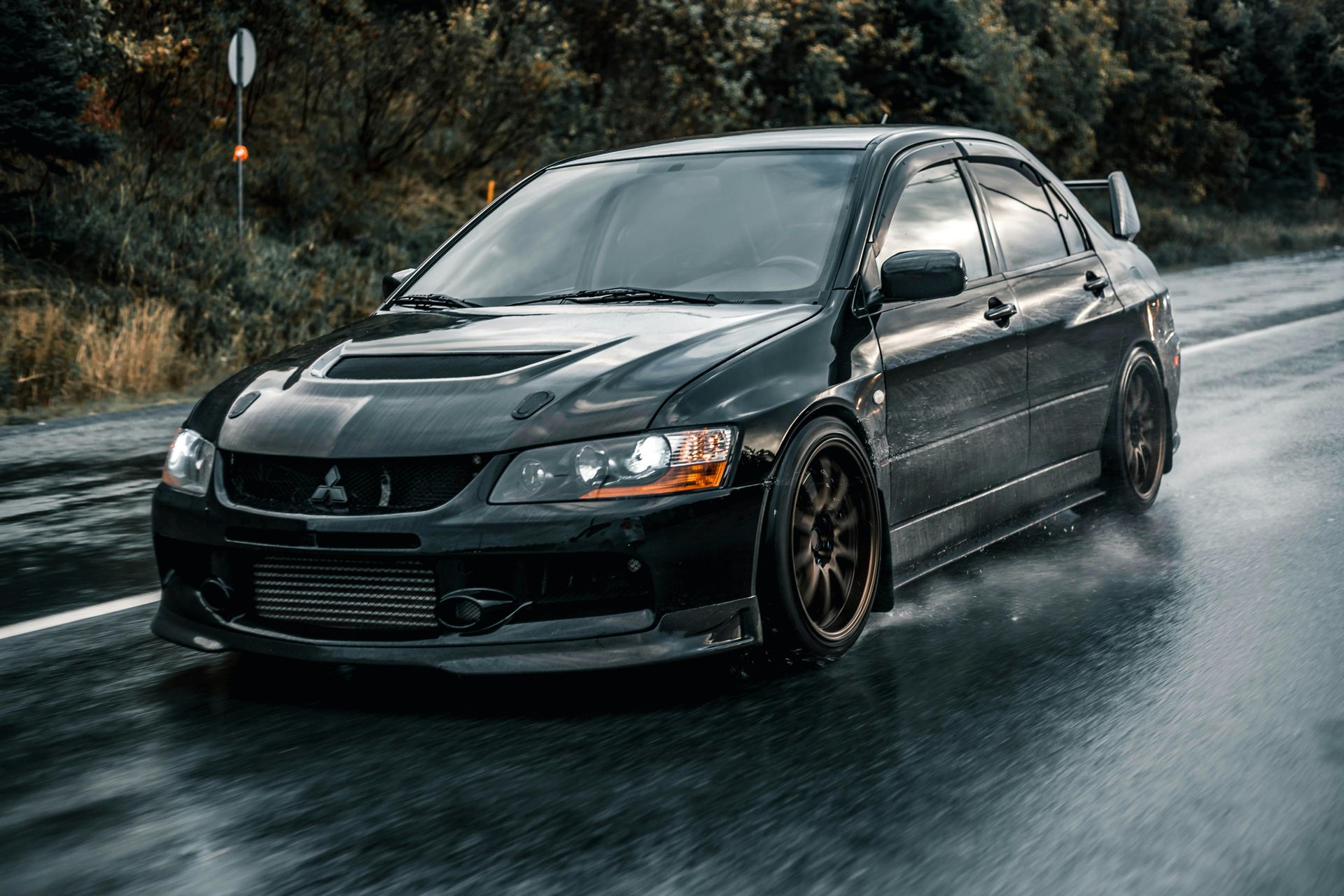 A black car is driving down a wet road.