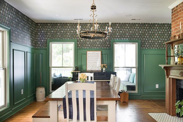 Elegant dining room with green paneled walls, patterned wallpaper, chandelier, and a central table with striped chair.