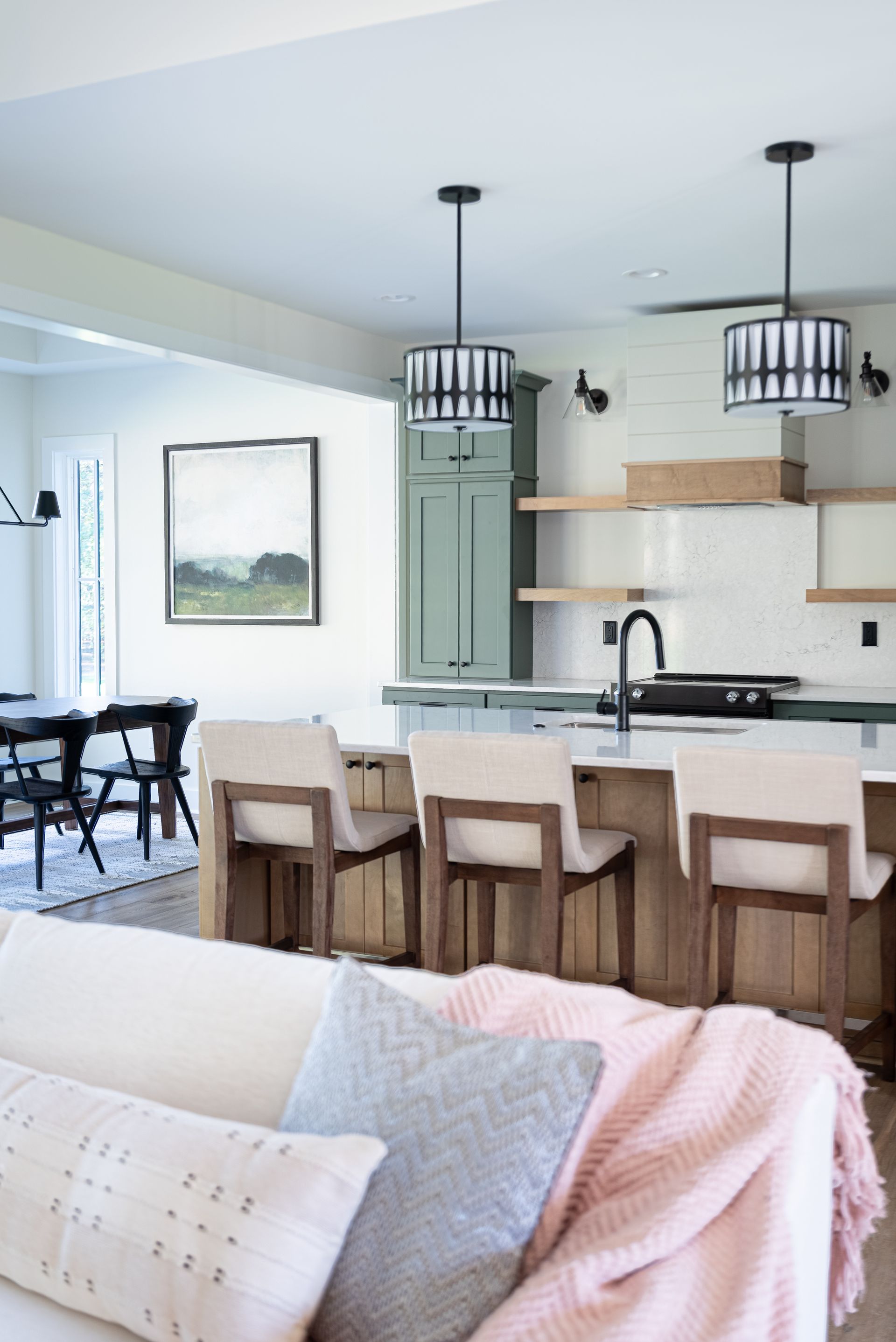 Bright modern kitchen and dining area with island, black pendant lights, and a pink throw on a sofa.
